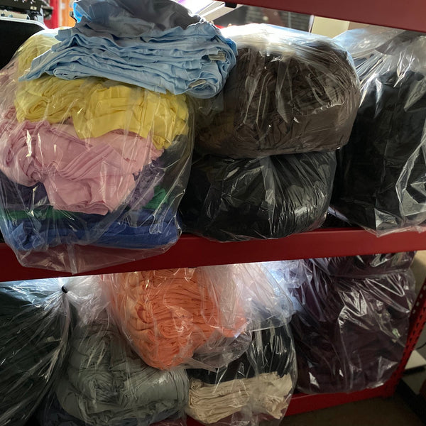 Bagged tees in yellow, pink, blue, orange and black stacked on red shelving at RVA Threads screen printing, Virginia