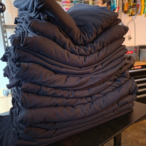Tall stack of folded black t-shirts squared up on the work table at RVA Threads screen printing, Virginia