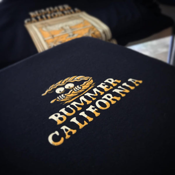 Bummer California logo in gold and white ink on a navy tee, laid flat at RVA Threads screen printing, Virginia