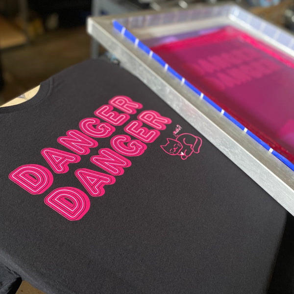 Danger Danger tee in pink ink on black Bella+Canvas 3001 on the press beside the pink ink screen at RVA Threads screen printing, Virginia