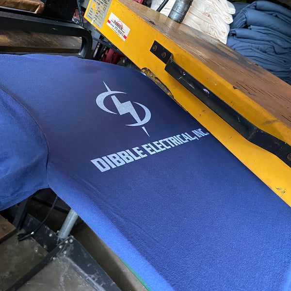 Dibble Electrical, Inc. logo in white ink on a blue tee on the press at RVA Threads screen printing, Virginia