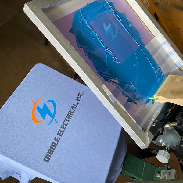 Dibble Electrical screen with blue ink raised over a printed gray tee on the press at RVA Threads screen printing, Virginia