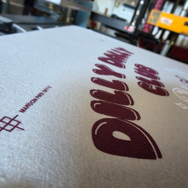 Close up of the Dilly Dally Club print in maroon ink on a Sand Gildan 2000 tee at RVA Threads screen printing, Virginia