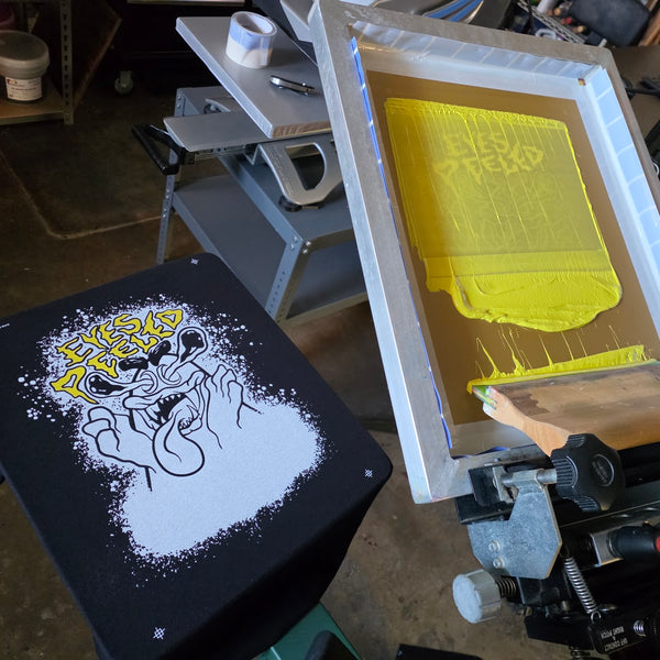 Eyes Peeled white underbase and yellow lettering on a black tee, yellow screen raised on the press at RVA Threads screen printing, Virginia