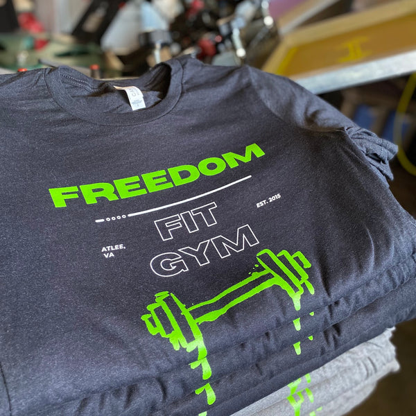 Freedom Fit Gym logo in neon green and white ink on charcoal tees, stacked at RVA Threads screen printing, Virginia
