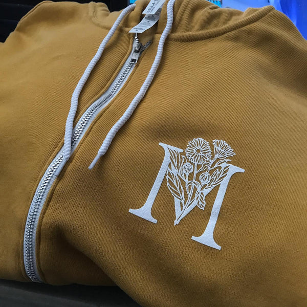 Hamilton Mercantile M monogram in white ink on a tan zip hoodie at RVA Threads screen printing, Virginia
