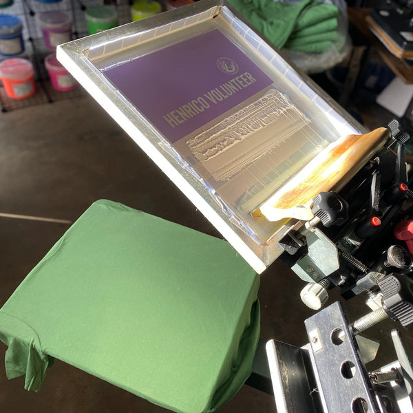 Henrico Volunteer screen raised over a green tee on the press at RVA Threads screen printing, Virginia
