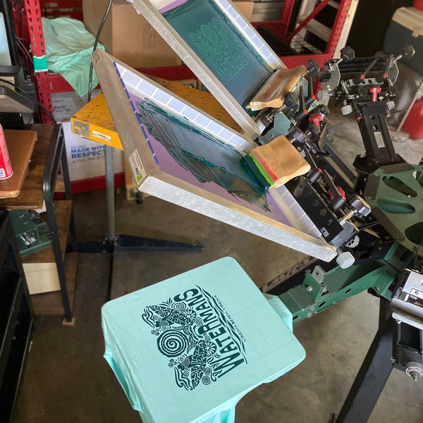Mint tee on the press with the screens raised for a detailed white ink design at RVA Threads screen printing, Virginia