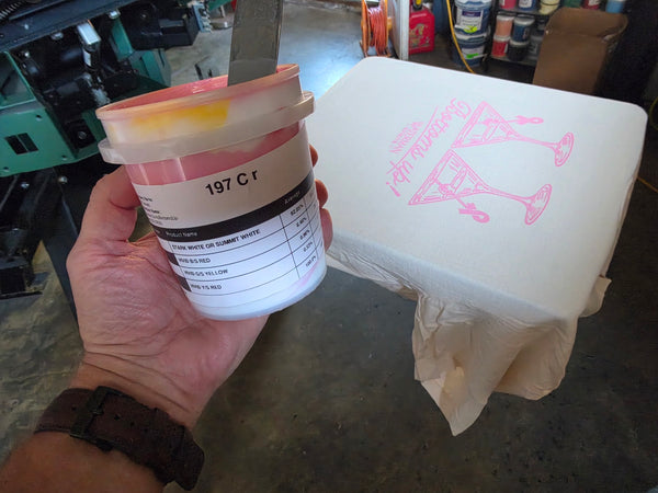 Pantone 197 C pink ink mixed for Waterman Spirits Bottoms Up, held next to the print on an Ivory tee at RVA Threads screen printing, Virginia