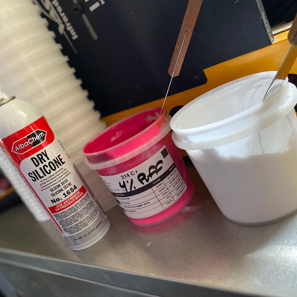 Tub of pink ink, a can of dry silicone spray and a bucket of white ink on the bench at RVA Threads screen printing, Virginia