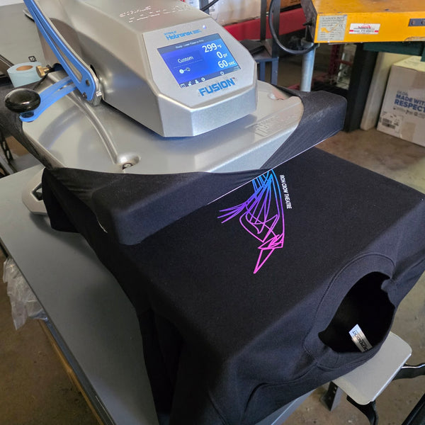 Purple, pink and blue bird print on a black tee resting on the Fusion heat press at RVA Threads screen printing, Virginia
