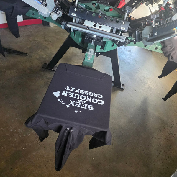 Seek and Conquer CrossFit print in white ink on a Black Champion S700 hoodie on the press platen at RVA Threads screen printing, Virginia