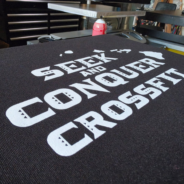 Close up of the Seek and Conquer CrossFit print in white ink on a Black Champion S700 hoodie at RVA Threads screen printing, Virginia