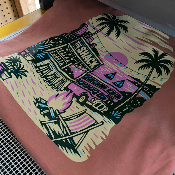 The Shack beach scene printed in full color on a peach tee on the press pallet at RVA Threads screen printing, Virginia