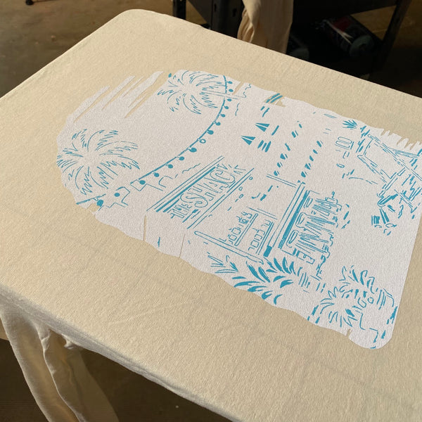 The Shack beach scene white underbase and teal first color on a natural tee on the pallet at RVA Threads screen printing, Virginia
