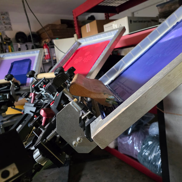 Three screens loaded on the manual press with the squeegee resting in the front screen at RVA Threads screen printing, Virginia