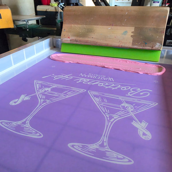 Waterman Spirits Bottoms Up screen with a bead of pink ink and a wood squeegee on the press at RVA Threads screen printing, Virginia