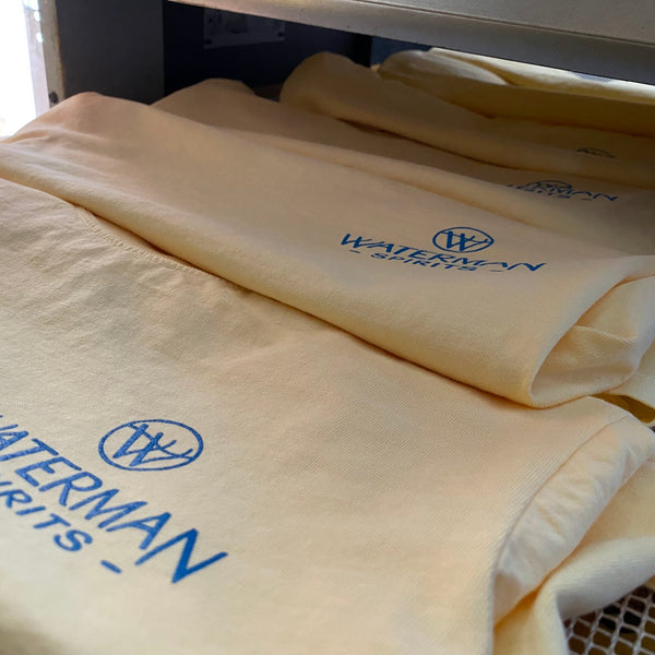 Waterman Spirits logo in blue ink on natural tees, folded and stacked at RVA Threads screen printing, Virginia