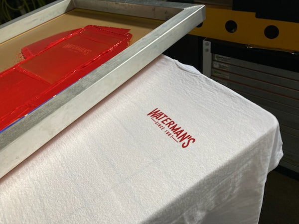 Waterman's left chest logo in red ink on a white tee with the red screen raised on the press at RVA Threads screen printing, Virginia