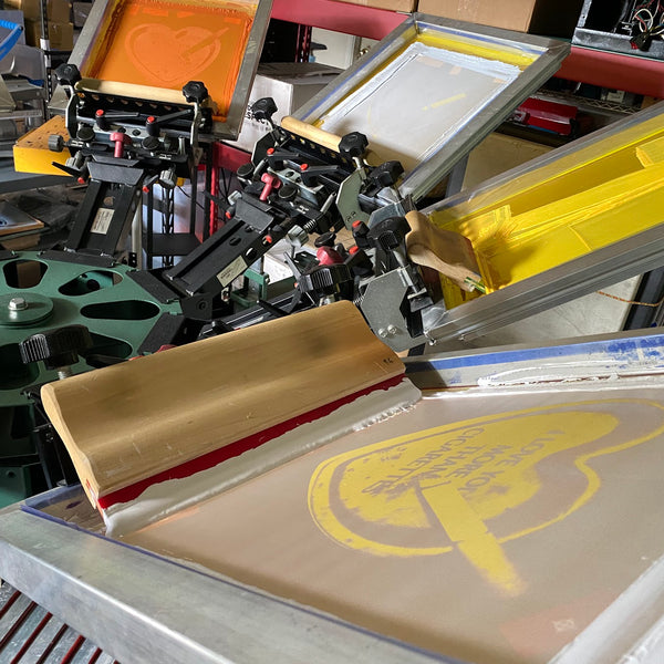 Yellow ink screens loaded on the press with a squeegee ready for the next pull at RVA Threads screen printing, Virginia