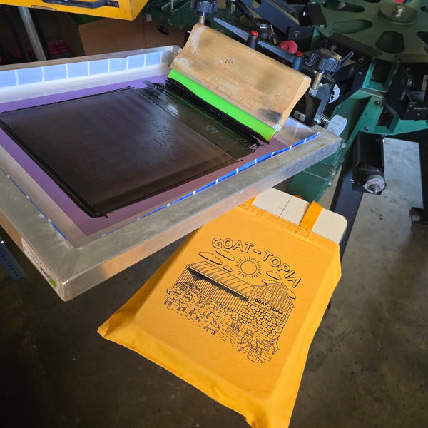 Goat-Topia tote bag on the press with the screen raised at RVA Threads screen printing, Virginia