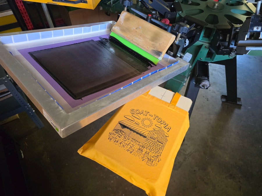 Goat-Topia tote bag on the press with the screen raised at RVA Threads screen printing, Virginia
