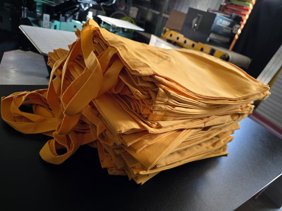 Finished Goat-Topia gold tote bags stacked and ready for pickup at RVA Threads screen printing, Virginia