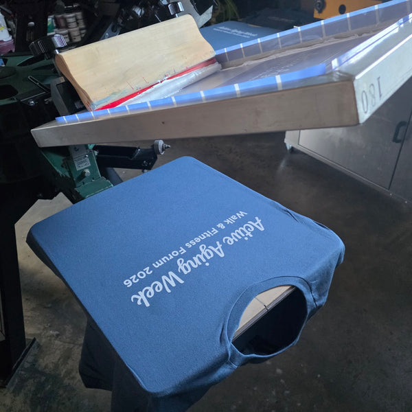 Active Aging Week Walk and Fitness Forum 2026 tee in blue with white ink on the press, screen raised at RVA Threads screen printing, Virginia