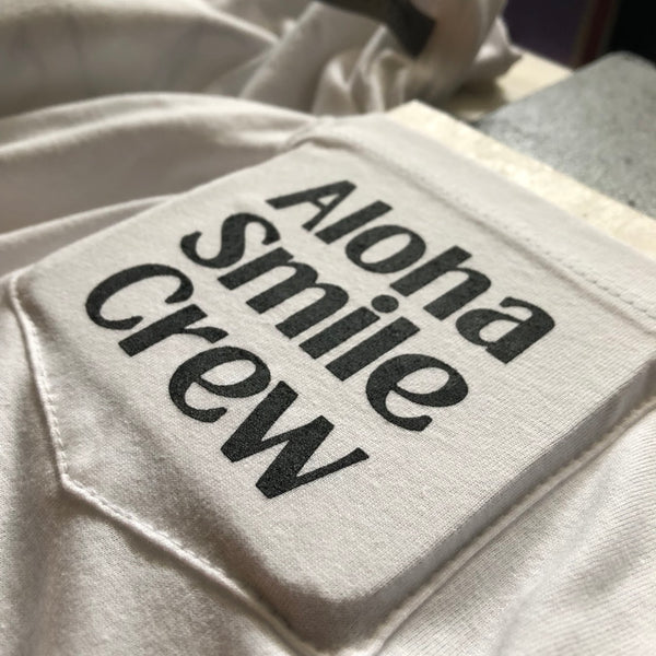 Aloha Smile Crew lettering in black ink on a white pocket tee, close up at RVA Threads screen printing, Virginia