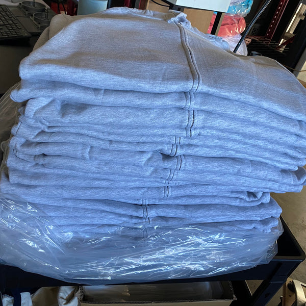 Stack of blank chalky blue tees folded on a plastic bag beside the press at RVA Threads screen printing, Virginia