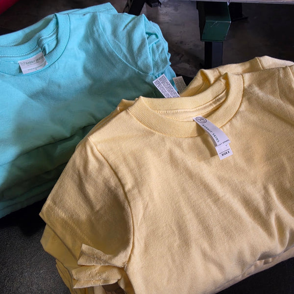 Stacks of blank mint and yellow t-shirts beside the press, ready to print at RVA Threads screen printing, Virginia