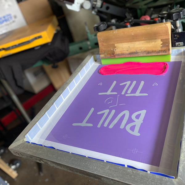 Built to Tilt screen with a squeegee and pink ink on the press, ready for the next shirt at RVA Threads screen printing, Virginia