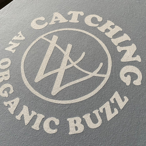 Catching An Organic Buzz logo in white ink on a charcoal tee, close up at RVA Threads screen printing, Virginia