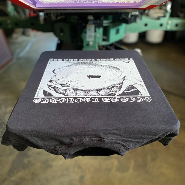 Circular eye graphic in white ink on a black tee on the press pallet at RVA Threads screen printing, Virginia