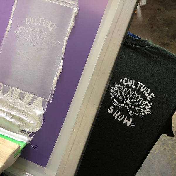 Culture Show lotus design in white ink on a black tee beside the screen at RVA Threads screen printing, Virginia