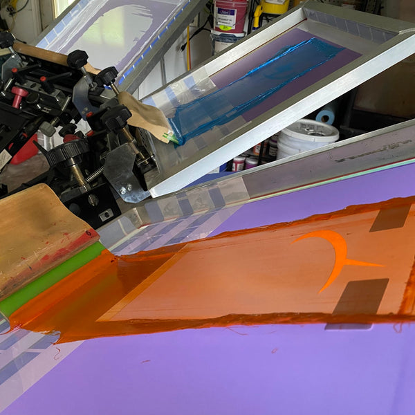 Orange ink flooded across the Dibble Electrical lightning logo screen with the squeegee at RVA Threads screen printing, Virginia