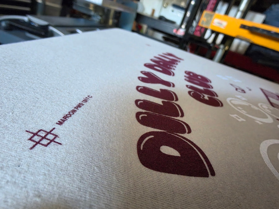 Close up of the Dilly Dally Club print in maroon ink on a Sand Gildan 2000 tee at RVA Threads screen printing, Virginia