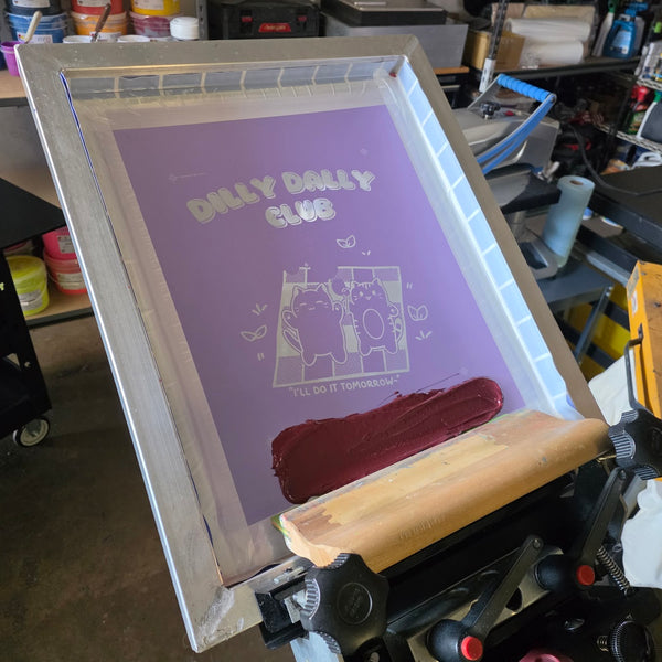 Dilly Dally Club screen flooded with maroon ink and a wood squeegee on the press at RVA Threads screen printing, Virginia