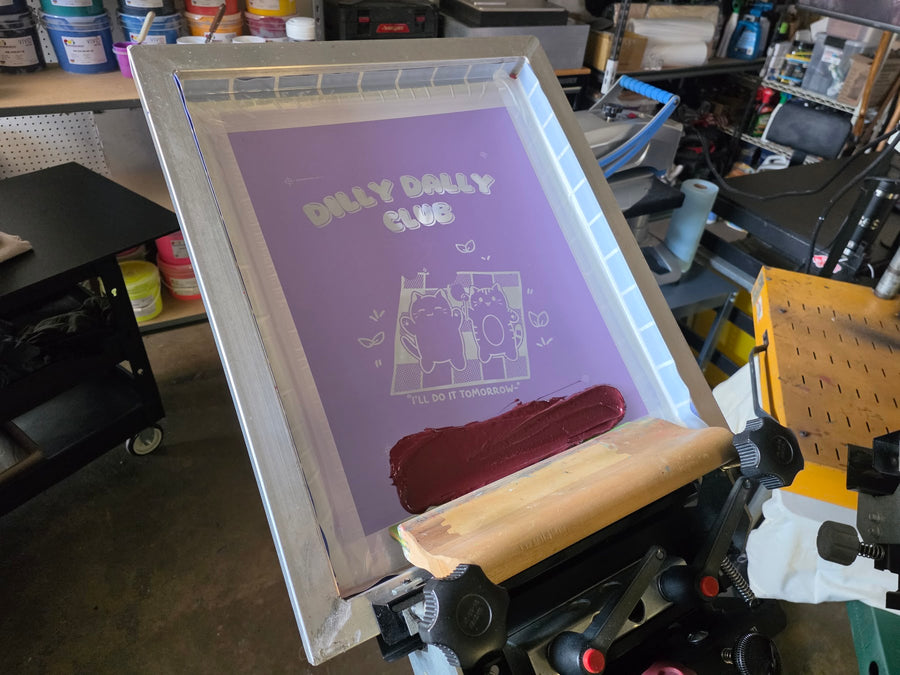 Dilly Dally Club screen flooded with maroon ink and a wood squeegee on the press at RVA Threads screen printing, Virginia