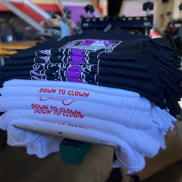 Down To Clown tees in white, purple and black, stacked after printing at RVA Threads screen printing, Virginia