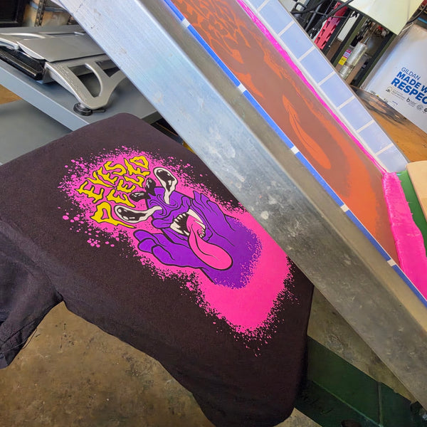 Eyes Peeled print on a Black Comfort Colors 1717 tee on the platen with the pink screen lifted at RVA Threads screen printing, Virginia
