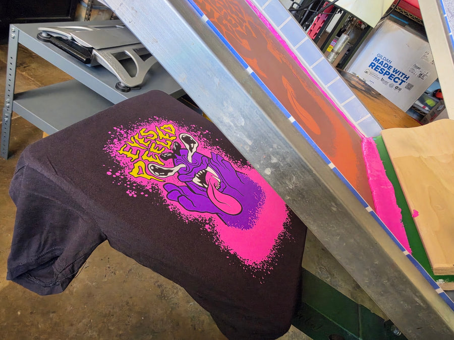 Eyes Peeled print on a Black Comfort Colors 1717 tee on the platen with the pink screen lifted at RVA Threads screen printing, Virginia