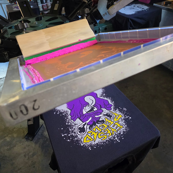 Eyes Peeled screen flooded with pink ink over a Black Comfort Colors 1717 tee on the press at RVA Threads screen printing, Virginia