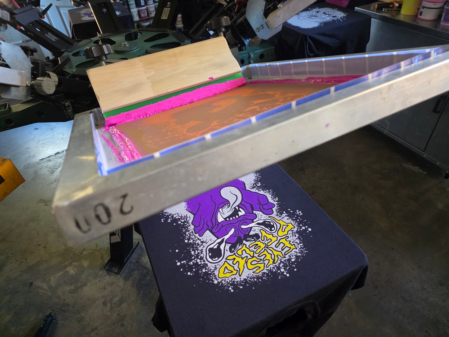 Eyes Peeled screen flooded with pink ink over a Black Comfort Colors 1717 tee on the press at RVA Threads screen printing, Virginia