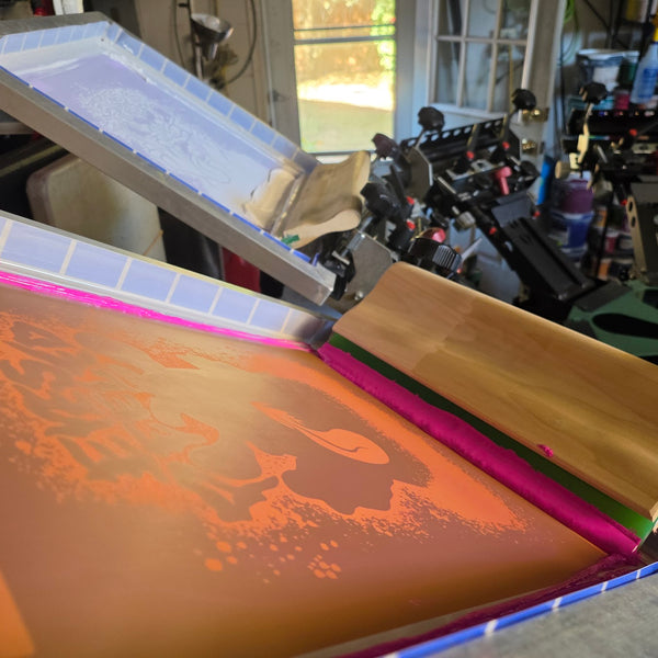 Eyes Peeled pink ink screen and wood squeegee on the press, white underbase screen raised behind at RVA Threads screen printing, Virginia