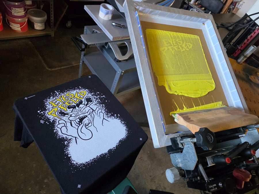 Eyes Peeled white underbase and yellow lettering on a black tee, yellow screen raised on the press at RVA Threads screen printing, Virginia