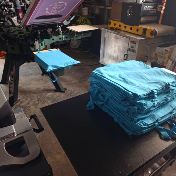 George's Mill Farm Do You Know Where Your Kids Are screen raised over turquoise tote bags on the press at RVA Threads screen printing, Virginia
