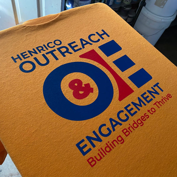 Henrico Outreach & Engagement logo in navy and red ink on a gold tee at RVA Threads screen printing, Virginia