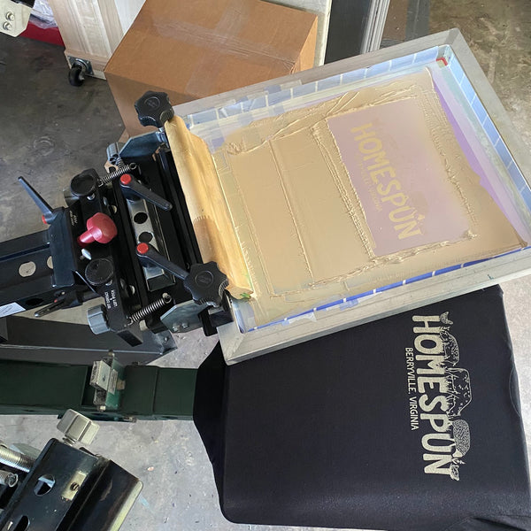 Homespun black tee printed in white ink beside the screen on the press at RVA Threads screen printing, Virginia