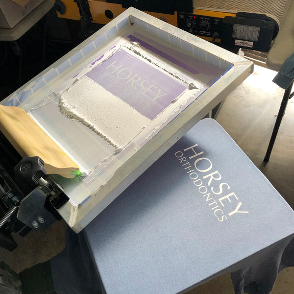 Horsey Orthodontics screen raised over a printed gray tee on the press at RVA Threads screen printing, Virginia